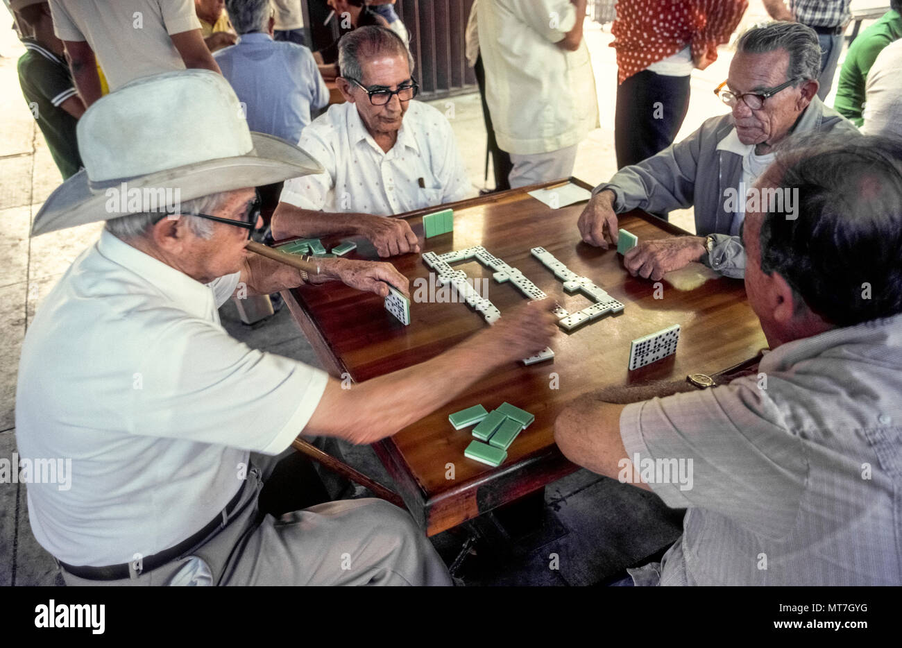 an-elderly-man-smoking-a-cuban-cigar-slaps-down-his-plastic-tile-on-a-wooden-table-during-a-noisy-game-of-dominoes-played-in-domino-park-in-little-havana-the-colorful-neighborhood-of-hispanic-culture-in-miami-florida-usa-located-at-the-corner-of-sw-8th-street-calle-ocho-and-15th-avenue-this-outdoor-social-center-is-officially-named-maximo-gomez-park-and-has-become-a-landmark-that-daily-draws-dozens-of-older-players-as-well-as-hundreds-of-tourists-historical-photo-MT7GYG.jpg